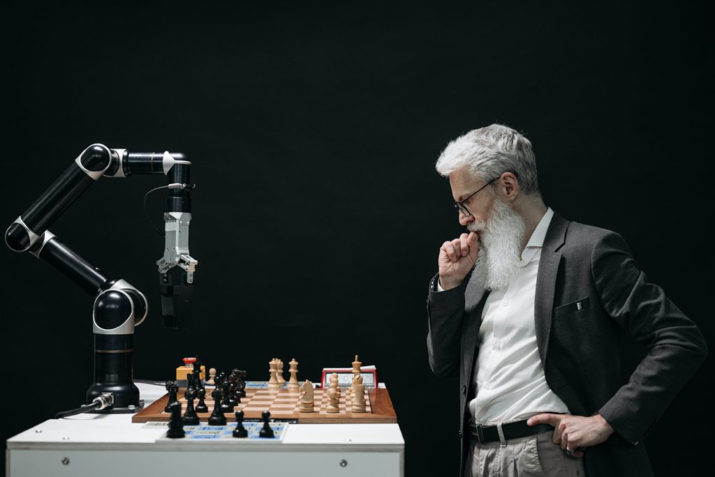 Young AI robot challenges elderly man to an intense game of chess on a wooden board, with both players strategizing their moves